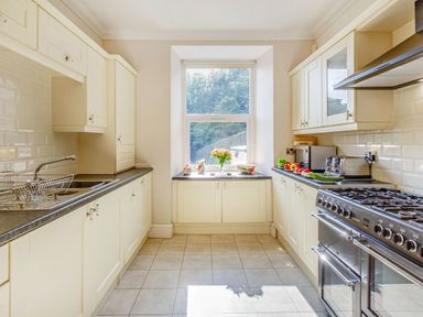 A kitchen with cream cabinets a window with flowers on the sill and a stainless steel stove at Menai View in Llanfairpwllgwyngyll near Beaumaris