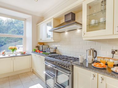 A kitchen with cream cabinets a gas stove a window with outdoor view and food items on the countertops at Menai View in Llanfairpwllgwyngyll near Beaumaris