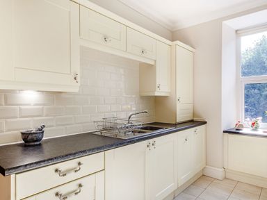 A kitchen with white cabinets a black countertop a sink with a drying rack and a window at Menai View in Llanfairpwllgwyngyll near Beaumaris