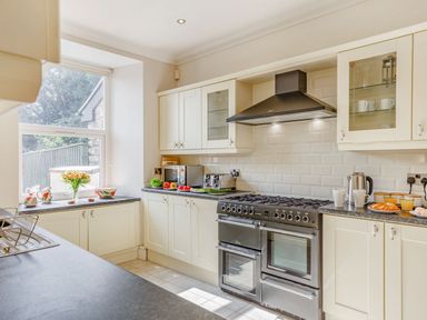 A kitchen with white cabinets a black stove and a window with flowers and kitchenware on the counters at Menai View in Llanfairpwllgwyngyll near Beaumaris