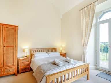 A bedroom with a wooden bed and wardrobe next to a glass door with curtains at Menai View in Llanfairpwllgwyngyll near Beaumaris