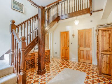 A hallway with wooden staircase wooden doors wooden cabinet and patterned tile floor at Menai View in Llanfairpwllgwyngyll near Beaumaris