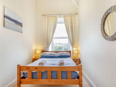 A bedroom with a wooden bed and two bedside tables next to a window with curtains at Menai View in Llanfairpwllgwyngyll near Beaumaris