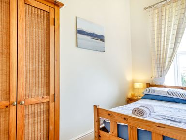 A bedroom with a wooden bed frame a nightstand with a lamp and a wooden wardrobe at Menai View in Llanfairpwllgwyngyll near Beaumaris