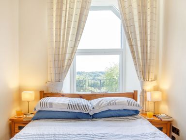 A bedroom with a wooden bed two pillows bedside tables lamps and a window with curtains at Menai View in Llanfairpwllgwyngyll near Beaumaris