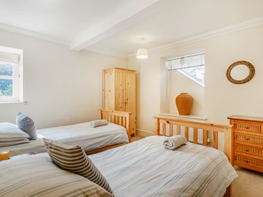 A bedroom with two single beds a wooden wardrobe a wooden chest of drawers and a window with a large vase at Menai View in Llanfairpwllgwyngyll near Beaumaris