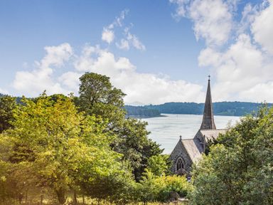 A church with a tall steeple surrounded by trees near a river at Menai View in Llanfairpwllgwyngyll near Beaumaris