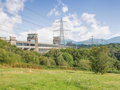 A green field with trees and a large bridge along with power lines and hills in the background at Menai View in Llanfairpwllgwyngyll near Beaumaris