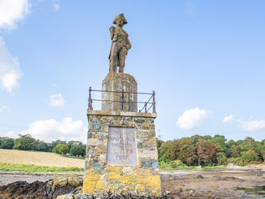 A stone statue of a man in uniform on top of a pedestal near a coastline with trees and grassy fields at Menai View in Llanfairpwllgwyngyll near Beaumaris