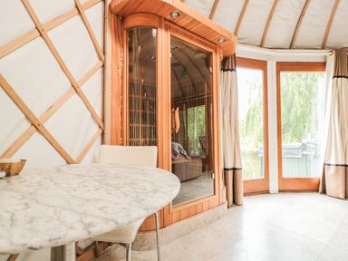 A marble table with a chair next to a wooden sauna and glass doors at Island Yurt in Beckford near Tewkesbury