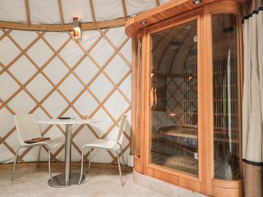 A small seating area with two chairs and a round table next to a wooden sauna at Island Yurt Beckford near Tewkesbury