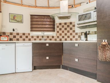 A kitchen with brown cabinets white appliances a microwave and a window with a brown blind at Island Yurt Beckford near Tewkesbury