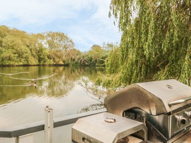 A barbecue grill on a deck overlooking a river with trees and ducks at Island Yurt in Beckford near Tewkesbury