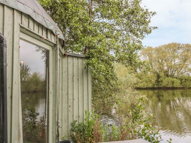 Side of a green wooden structure near a body of water with trees and vegetation around at Island Yurt in Beckford near Tewkesbury