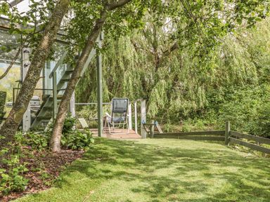 An outdoor space with a grassy area trees and a deck with chairs at Island Yurt in Beckford near Tewkesbury