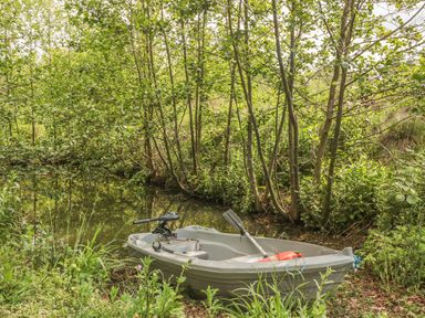 A small boat on a narrow creek surrounded by trees and greenery at Island Yurt in Beckford near Tewkesbury