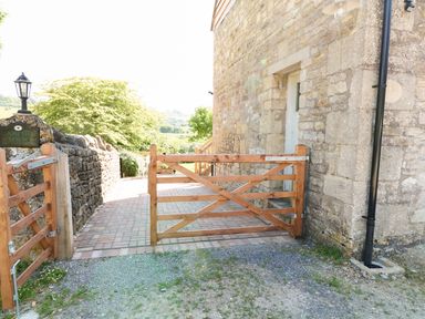 A wooden gate and stone wall next to a stone building with a pathway and greenery at The Loft at Lucott House in Bath