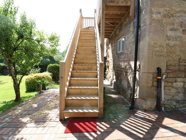 A wooden outdoor staircase leading to an upper floor attached to a stone building with a tree and bushes nearby at The Loft at Lucott House in Bath