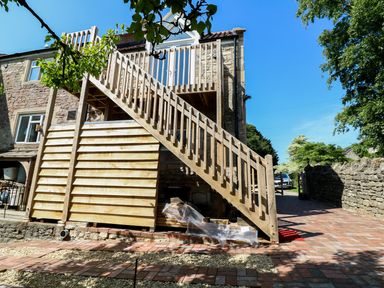 An exterior view of a stone building with wooden stairs leading to an upper door at The Loft at Lucott House in Bath