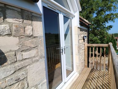 A small wooden balcony with railing and glass double doors on a stone building exterior at The Loft at Lucott House in Bath