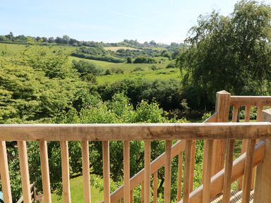 A wooden balcony railing overlooking green trees and hills at The Loft at Lucott House in Bath
