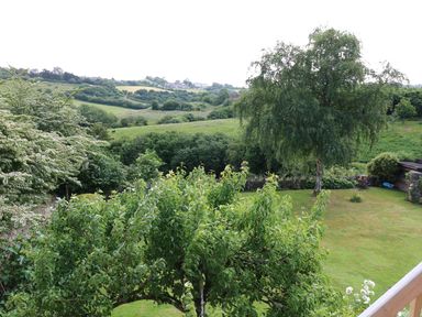 A garden with trees and grass overlooking green fields and hills at The Loft at Lucott House in Bath