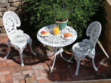 A white metal table with two chairs on a brick patio with croissants juice and a potted plant nearby at The Loft at Lucott House in Bath