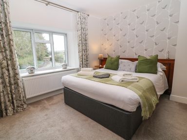 A bedroom with a bed with green pillows and a window with floral curtains at The Loft at Lucott House in Bath