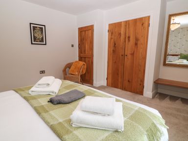 A bedroom with a bed covered by a green checkered blanket and folded towels wooden doors a rattan chair with an orange blanket and a mirror on the wall at The Loft at Lucott House in Bath
