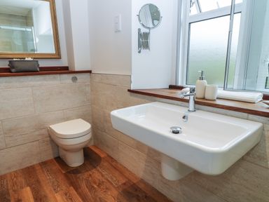 A bathroom with a wall-mounted sink and toilet and a window above the sink at The Loft at Lucott House in Bath
