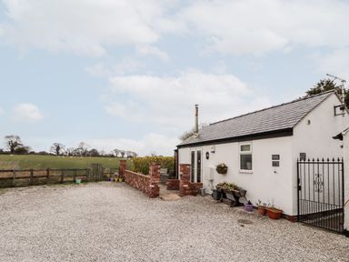A small white building with a gravel driveway and flower pots next to a fenced field at The Old Stable in Mold