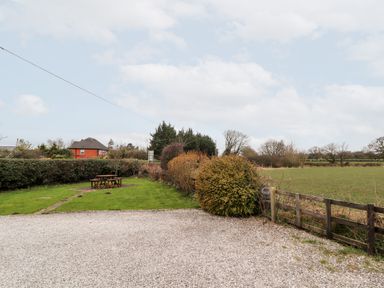 An outdoor area with a gravel ground, wooden fence, bushes, grass, trees, and a wooden picnic table at The Old Stable in Mold