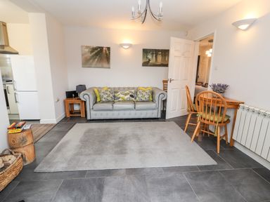 A living room with a grey sofa and cushions a wooden dining table with chairs and a rug on the floor at The Old Stable in Mold