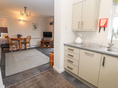 A kitchen area with cabinets and a sink next to a dining area with a wooden table and chairs at The Old Stable in Mold