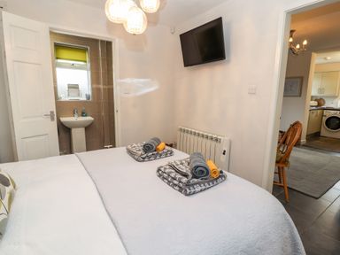 A bedroom with a bed, folded towels, a wall-mounted TV, a radiator, and doors leading to a bathroom and kitchen area at The Old Stable in Mold
