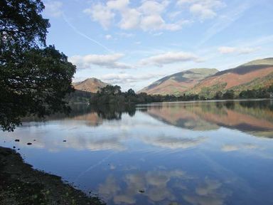 A lake with mountains and trees reflected in the water at High View Lodge in White Cross Bay near Troutbeck Bridge