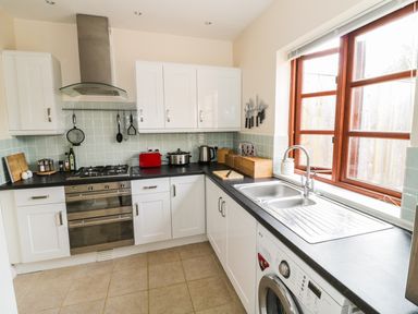 A kitchen with white cabinets a stainless steel oven and stove a red toaster and a sink under a window at The Old Dairy in Newnham-on-Severn