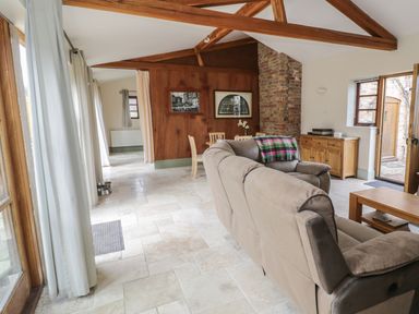 A living room with a beige sofa a wooden dining table wooden furniture exposed ceiling beams and a brick chimney at The Old Dairy in Newnham-on-Severn