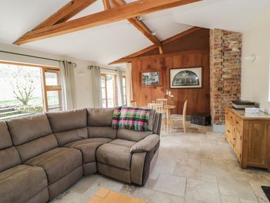 A living room with a sectional sofa wooden dining table and chairs wooden sideboard and exposed brick wall at The Old Dairy in Newnham-on-Severn