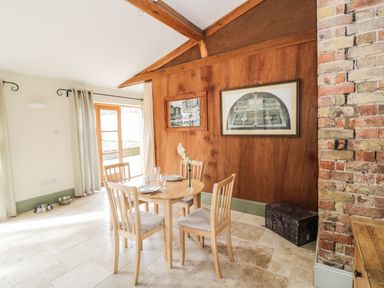 A dining area with wooden table and four chairs beside a wooden wall with framed pictures and a brick wall at The Old Dairy in Newnham-on-Severn