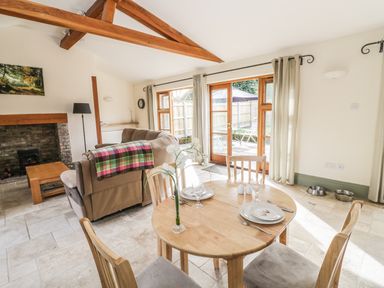 A dining area with a round wooden table set for two and a living room with a sofa and fireplace at The Old Dairy in Newnham-on-Severn