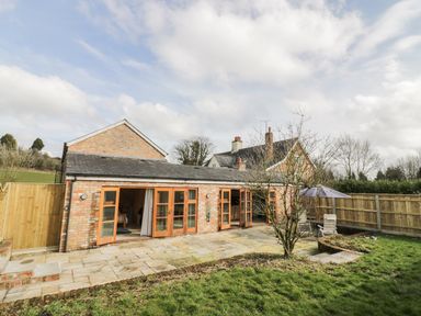 A brick house with wooden framed glass doors opening onto a stone patio and a garden with a tree and outdoor furniture at The Old Dairy in Newnham-on-Severn