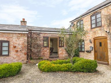 A brick exterior house with wooden door and windows surrounded by shrubs and gravel at The Old Dairy in Newnham-on-Severn