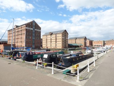 A marina with narrowboats docked along a quay and large brick warehouse buildings in the background at The Old Dairy in Newnham-on-Severn