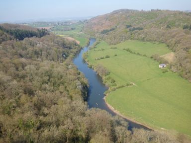 A river flowing through a valley with trees on one side and green fields with a small building on the other at The Old Dairy in Newnham-on-Severn