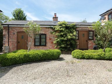 A brick building with two wooden doors and two windows with bushes and trees in front at The Old Dairy in Newnham-on-Severn