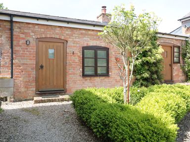 A brick exterior wall with two wooden doors two windows and green bushes in front at The Old Dairy in Newnham-on-Severn