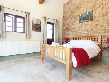 A bedroom with a wooden bed and red blanket against a brick wall at The Old Dairy in Newnham-on-Severn