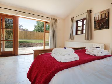 A bedroom with a bed covered with red blanket and white towels next to patio doors at The Old Dairy in Newnham-on-Severn