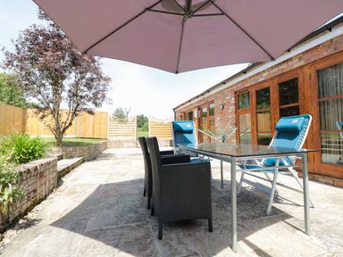 An outdoor patio with chairs a glass table and an umbrella next to a brick building at The Old Dairy in Newnham-on-Severn